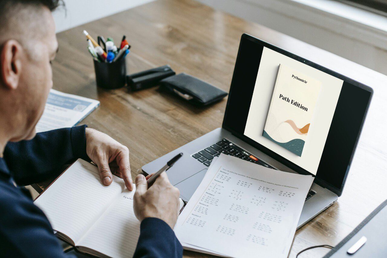 Person studying with a laptop displaying a course cover on a wooden desk.
