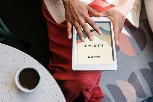 Person holding a tablet with a digital course cover displayed, sitting on a couch next to a coffee cup.